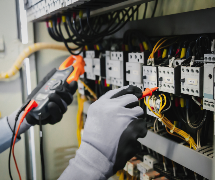 An electrician is working on an electrical panel with a multimeter.