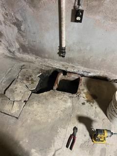 A hole in the floor of a basement with a drill and pliers.
