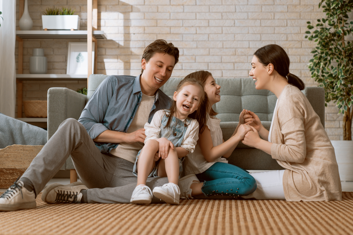 A family is sitting on the floor in a living room holding hands.