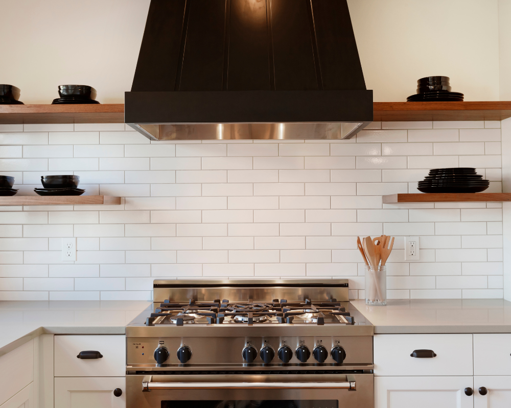 A kitchen with white cabinets and a stove with a black hood