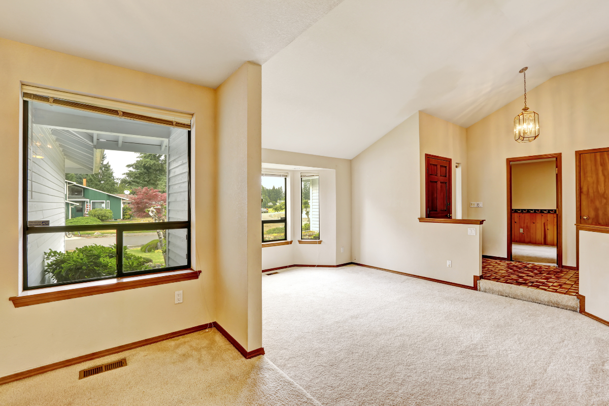 An empty living room with a large window and carpet.