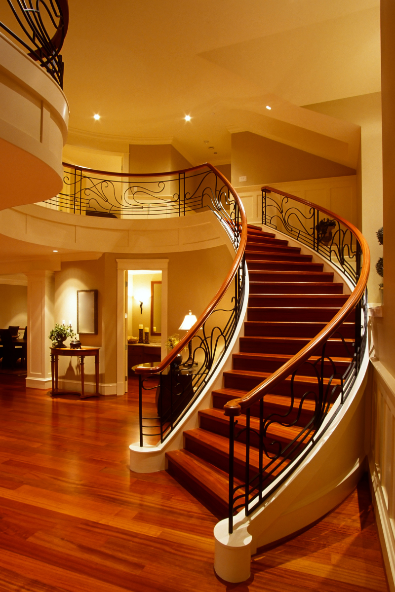 A curved staircase with red carpet and a wrought iron railing