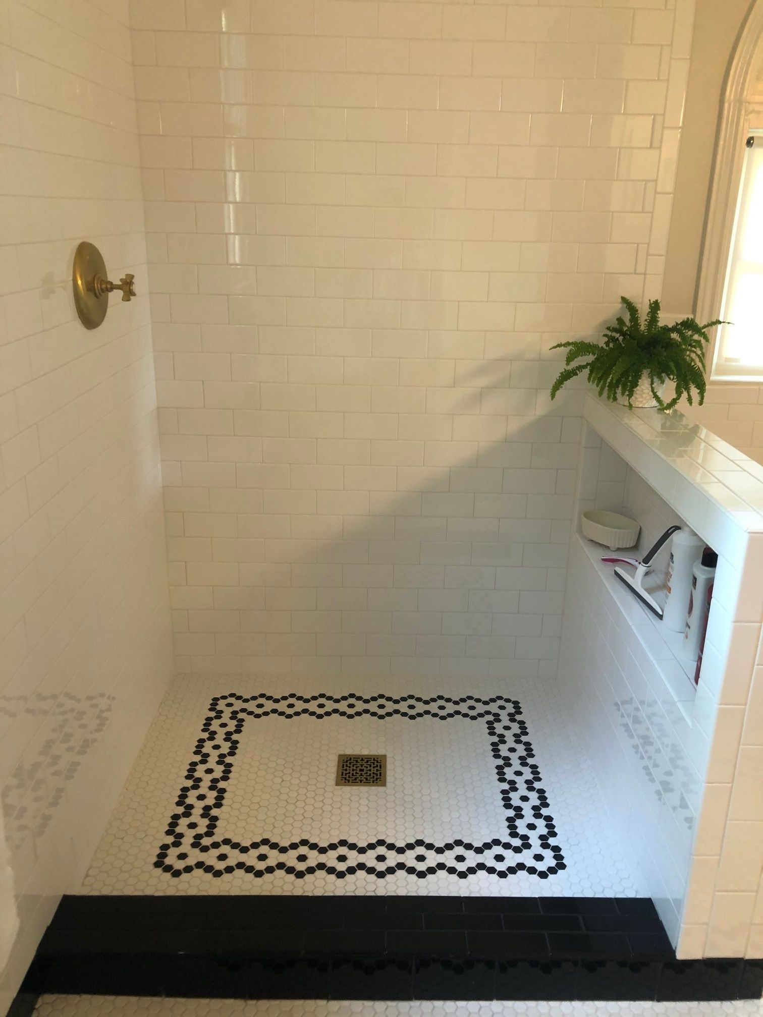 A bathroom with white tiles and a black and white mosaic floor