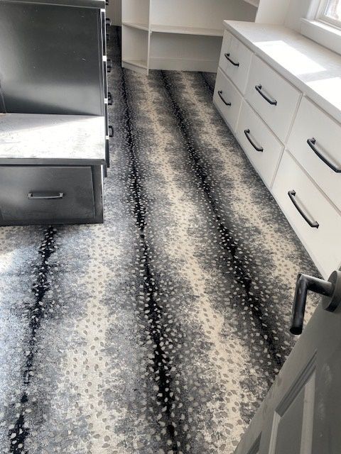 A walk in closet with a gray and white carpet and white drawers.