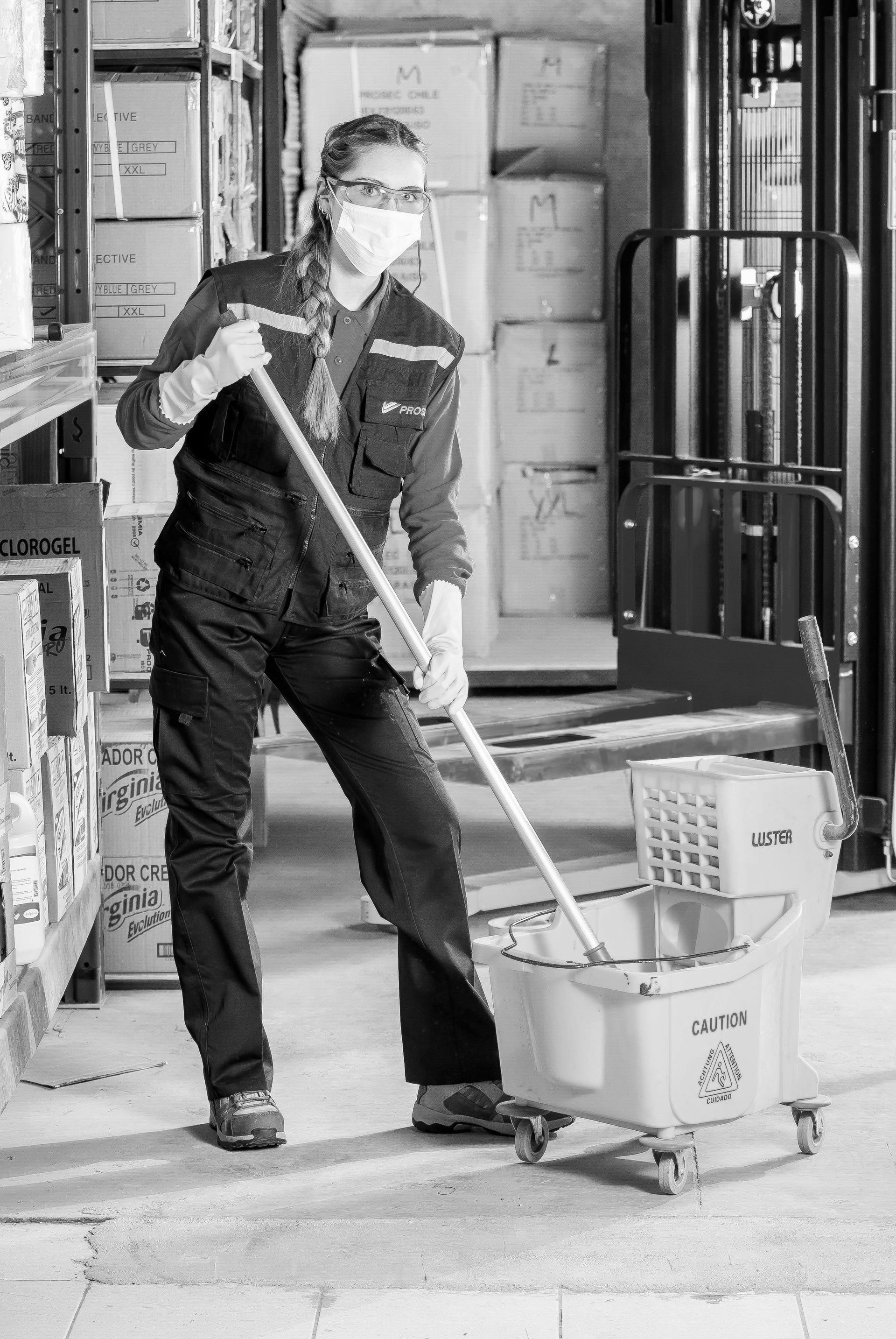 A woman wearing a mask is mopping the floor in a warehouse.