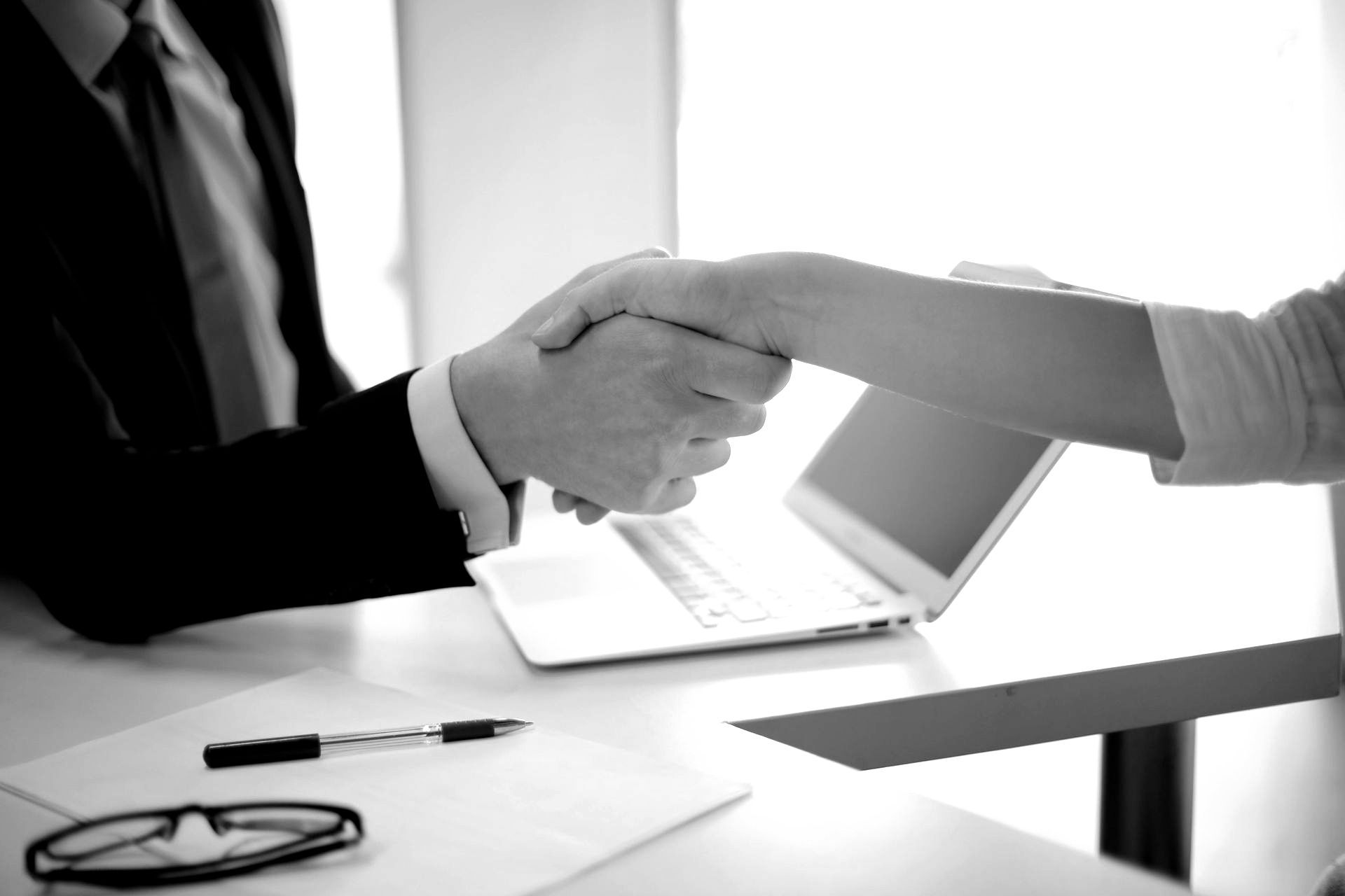 A man and a woman are shaking hands in front of a laptop.