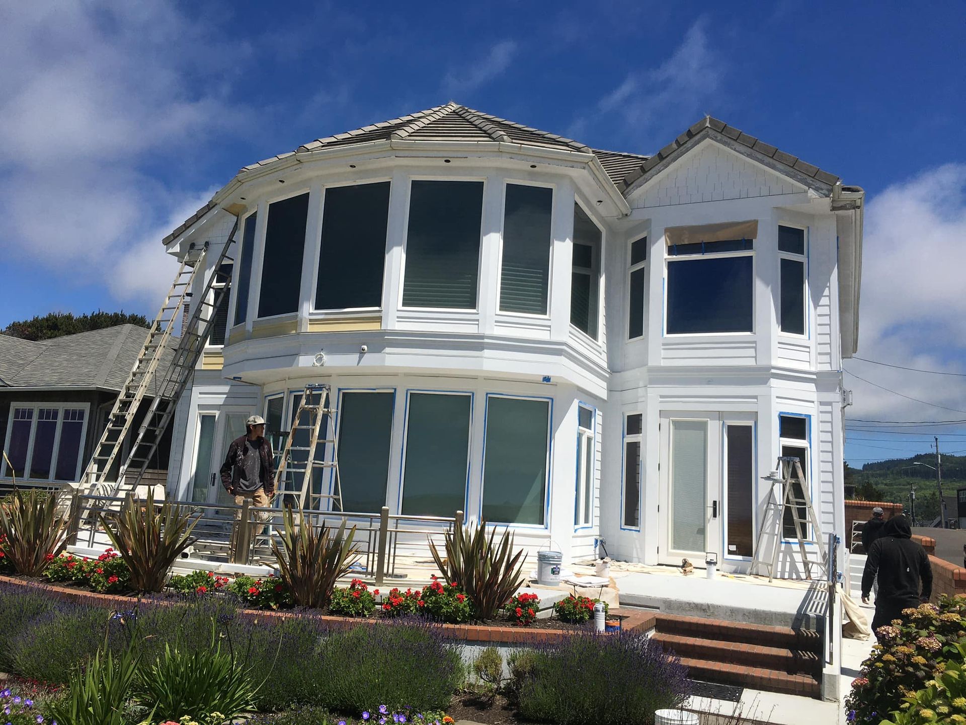 A large white house is being painted on a sunny day.