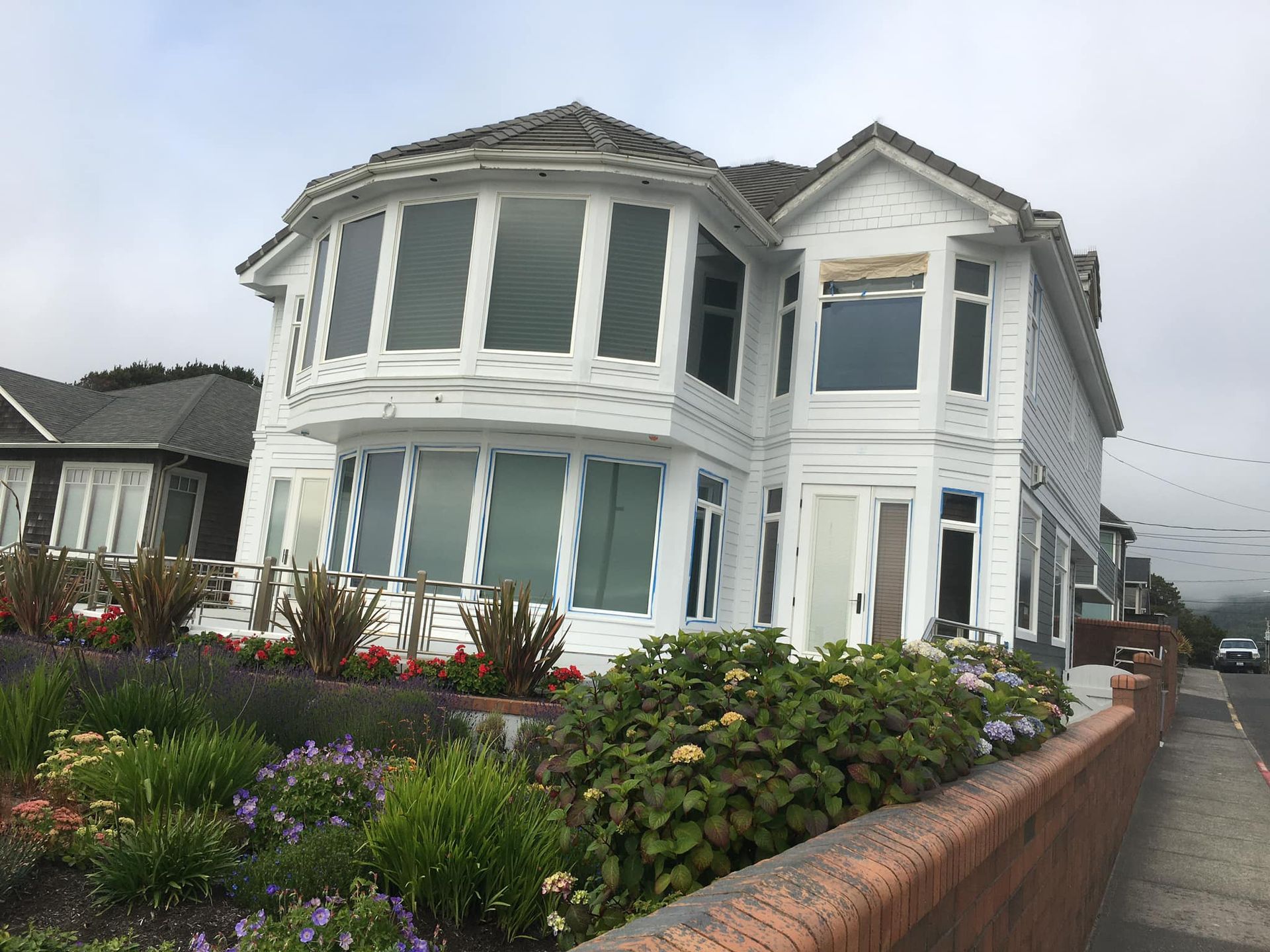 A large white house with a lot of windows is surrounded by flowers and bushes.