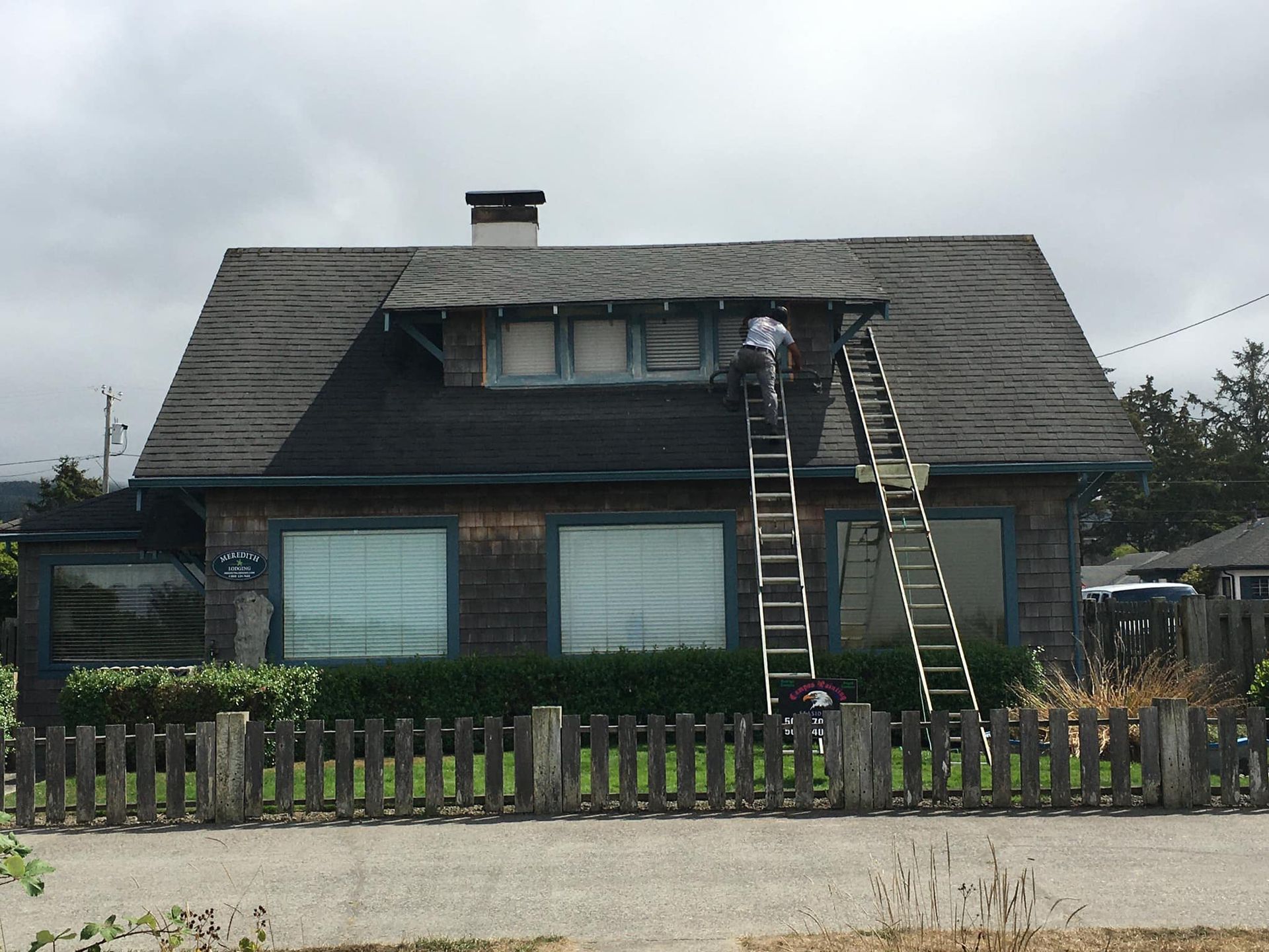 A man on a ladder is painting the roof of a house.