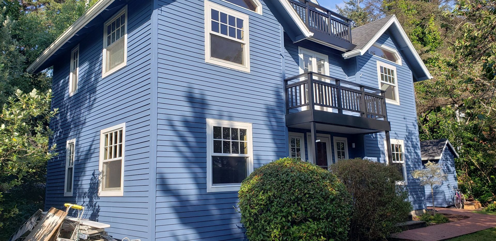 A large blue house with a balcony is surrounded by trees and bushes.