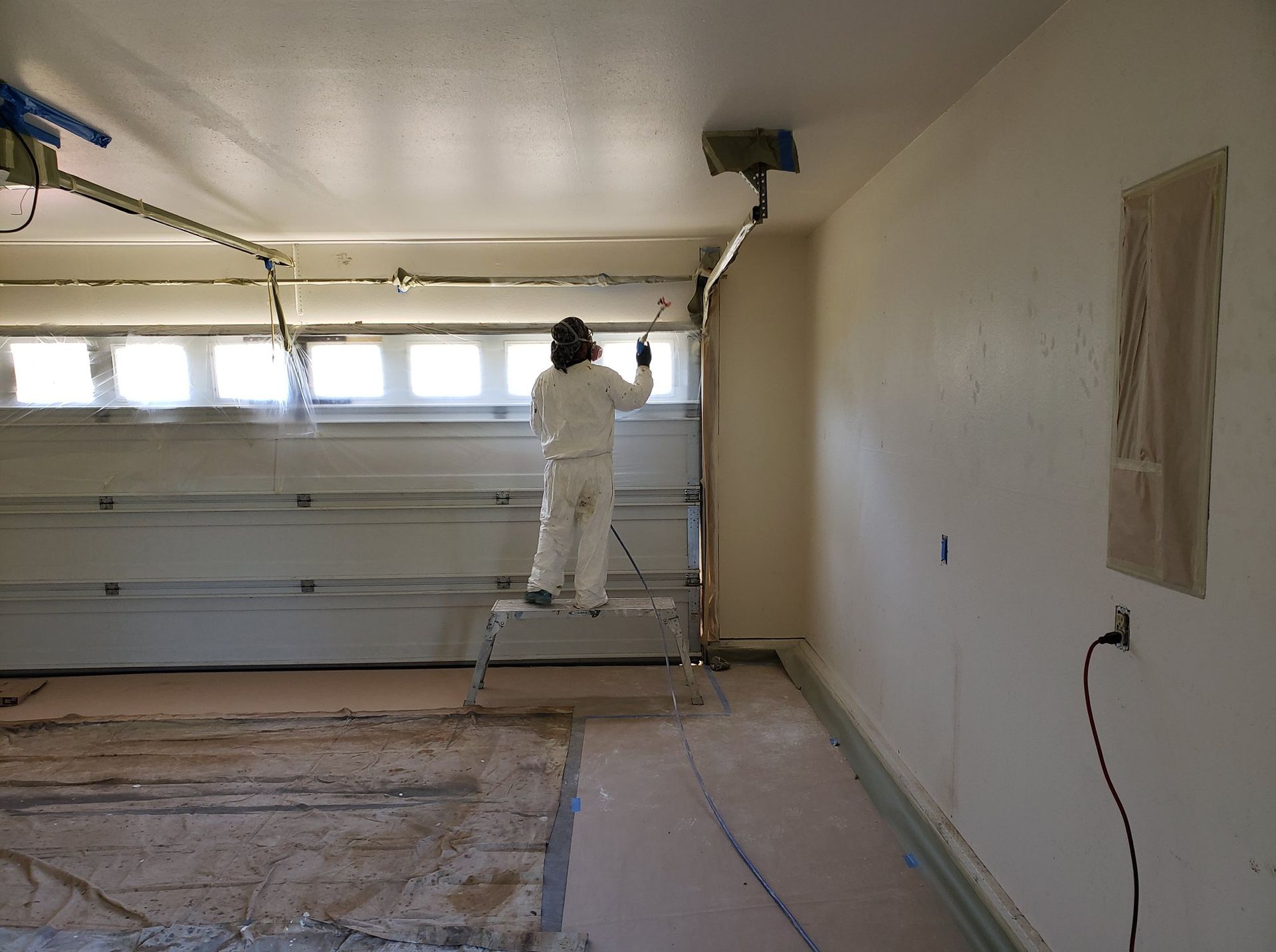 A man is standing on a ladder in a garage opening a garage door.