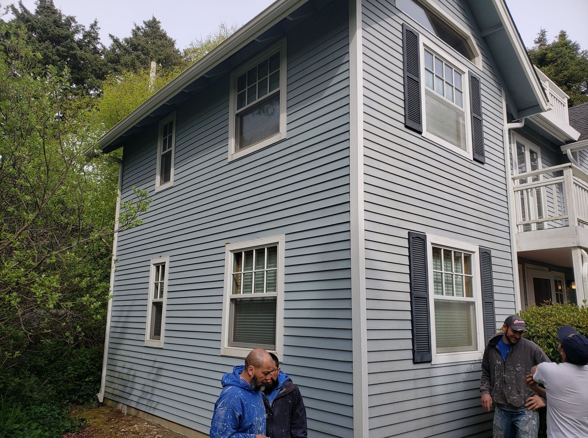 Three men are standing in front of a blue house.