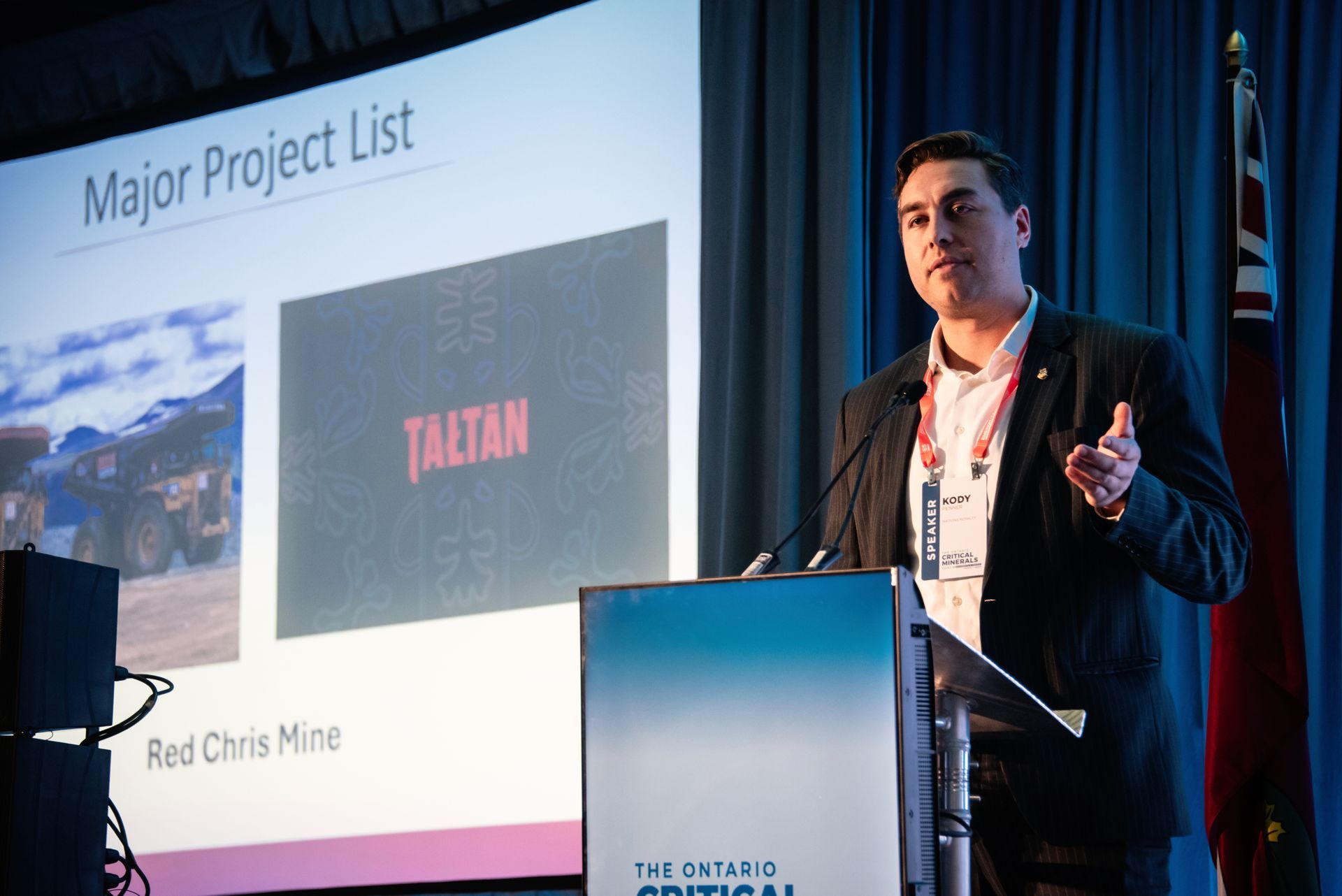 Man presenting at a conference, gesturing towards a slide with