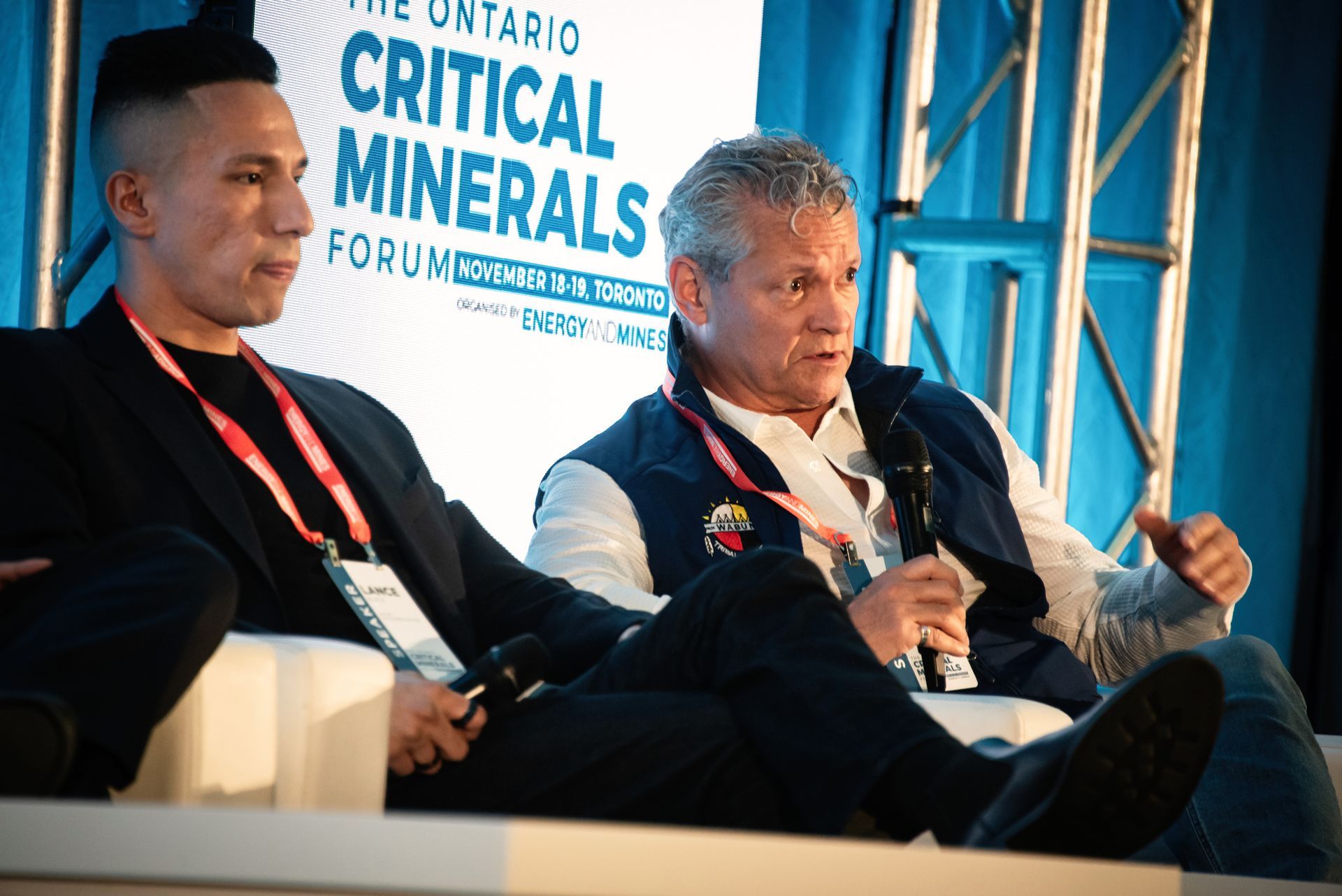 Two men at a panel discussion, in front of a blue backdrop, the words