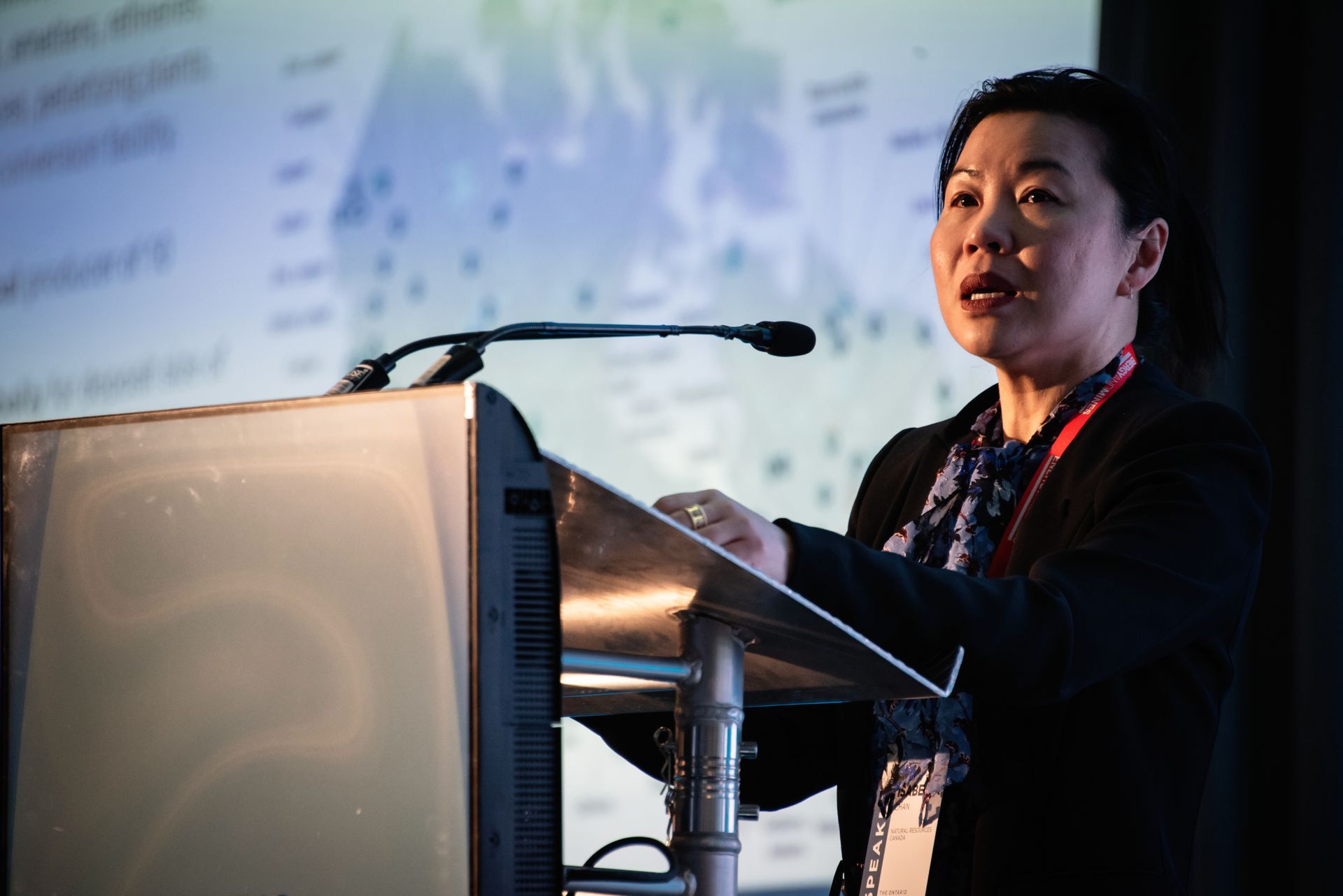 Isabella Chan from NRCan speaking at a podium, gesturing toward a screen with a world map and data during a presentation.