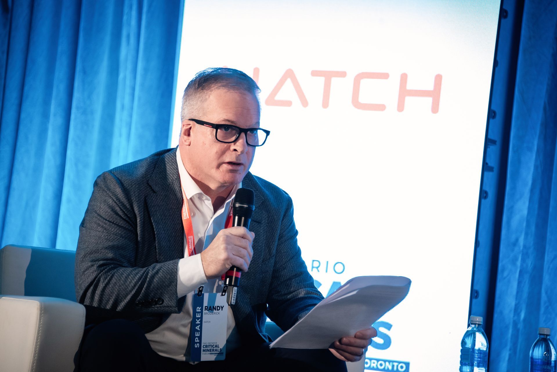 Hatch speaker into microphone, holding notes, at an event with a