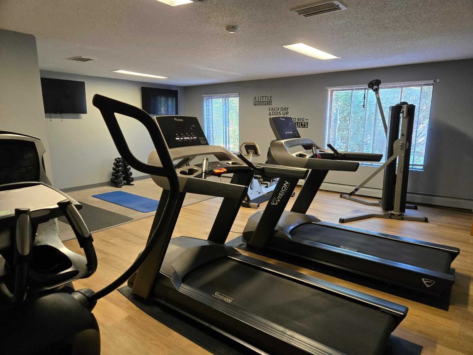Indoor community gym with treadmills, elliptical, weights, and a cable machine.