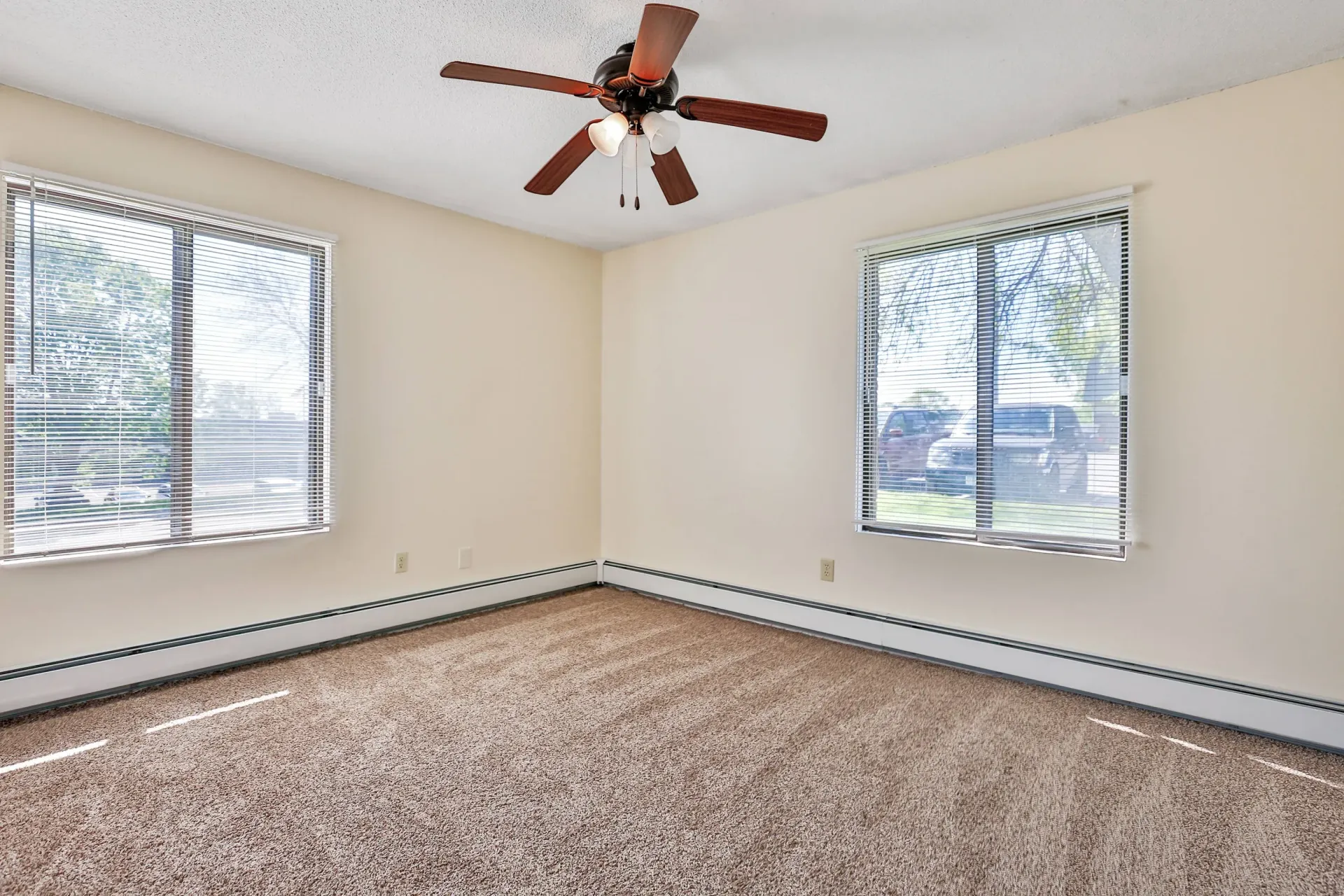 Empty living room with two windows, beige walls, and a ceiling fan.