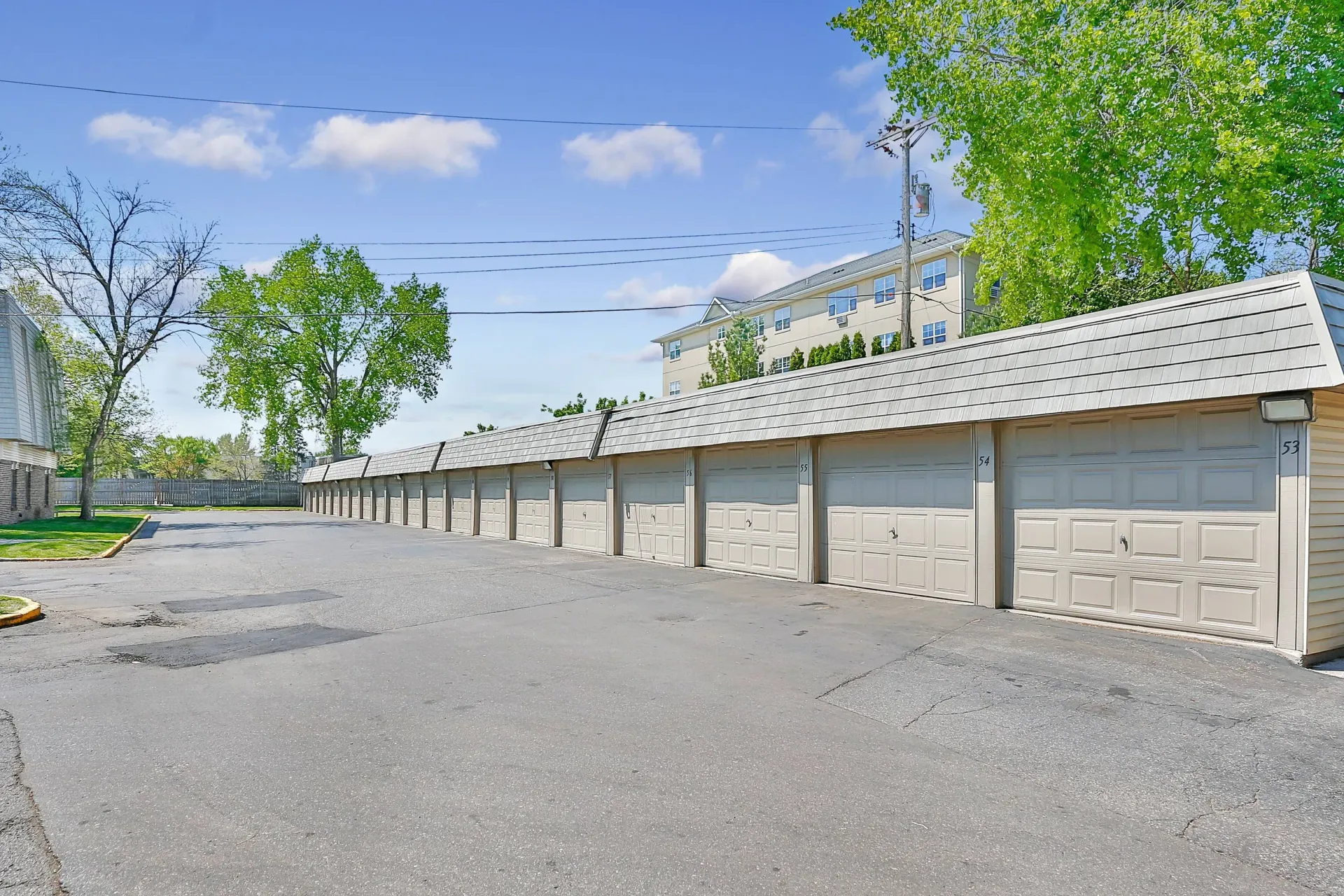 Row of beige garage doors along a paved driveway at an apartment community.