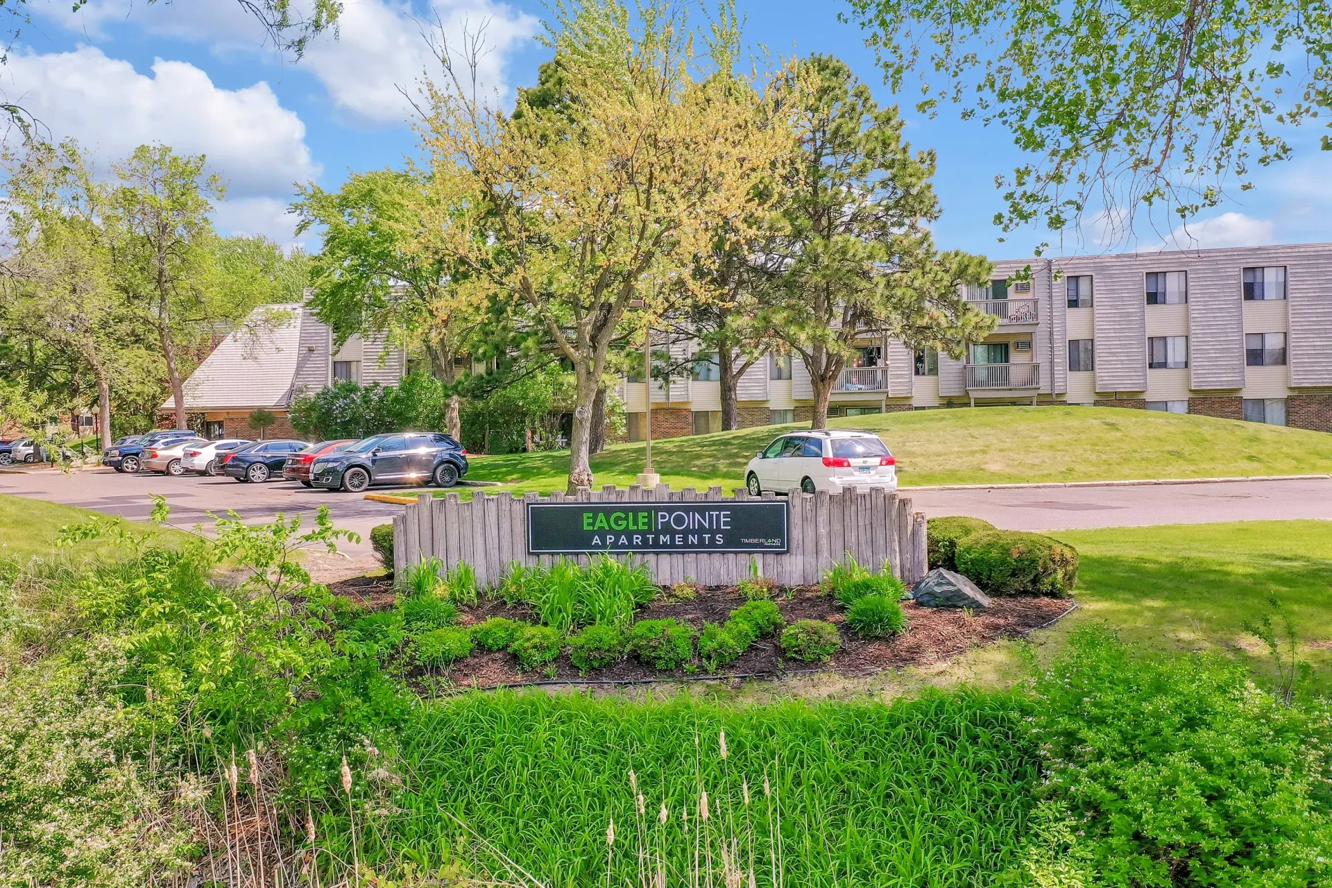 Exterior view of Eagle Pointe Apartments with landscaped entry, sign, and parked cars.