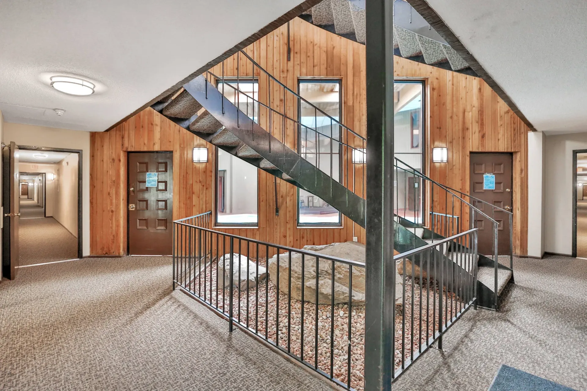 Interior of a residential building lobby with a metal staircase and wood paneling.
