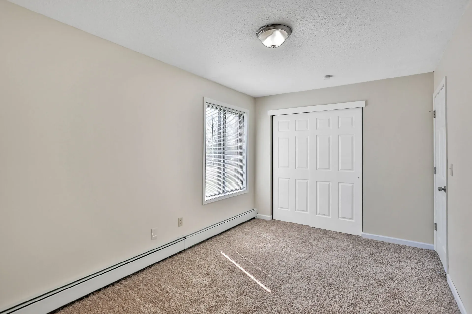 Empty beige bedroom with window and white sliding closet doors.