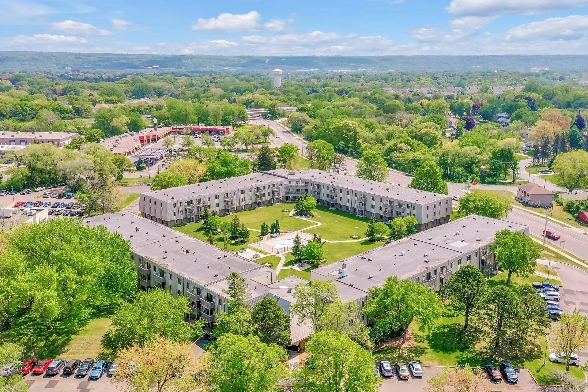 Aerial view of a light-colored apartment complex surrounded by trees and greenery under a blue sky at Eagle Point Apartments in West St. Paul, MN.