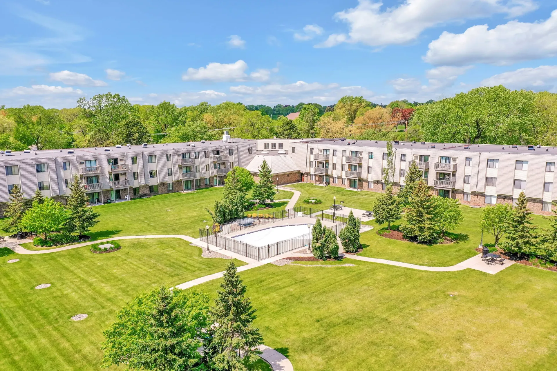 Aerial view of a residential complex with a pool in a central courtyard surrounded by green lawns and trees at Eagle Point Apartments in West St. Paul, MN.