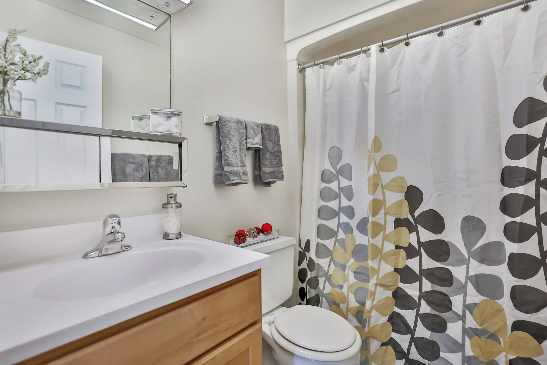 Bathroom with white sink, wood cabinet, shower curtain with leaf design, and gray towels at Eagle Point Apartments in West St. Paul, MN.