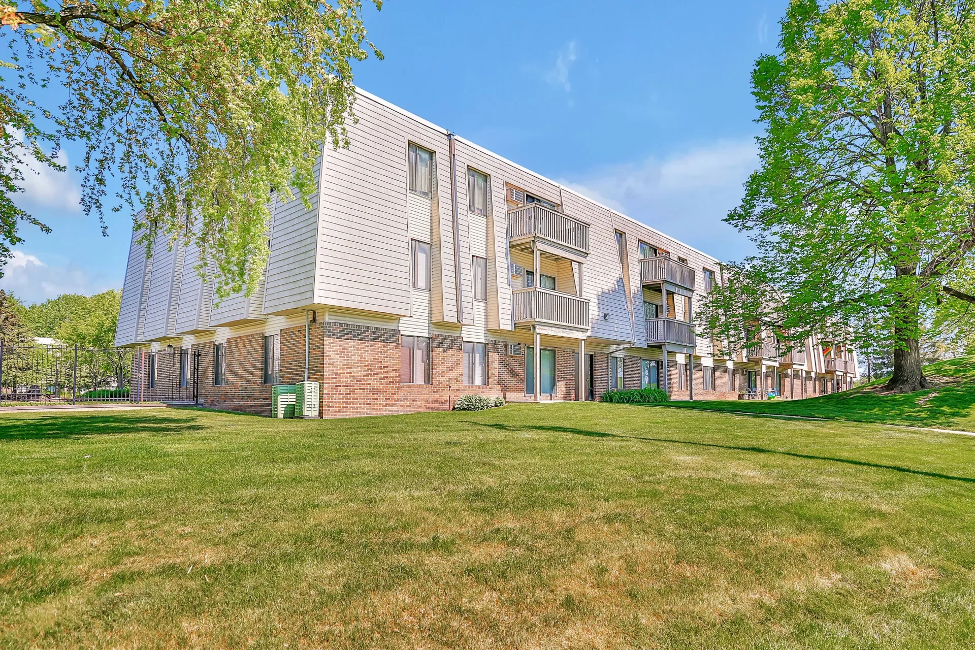 Multi-story apartment building with white perforated siding and balconies, set on a grassy lawn under a bright blue sky at Eagle Point Apartments in West St. Paul, MN.