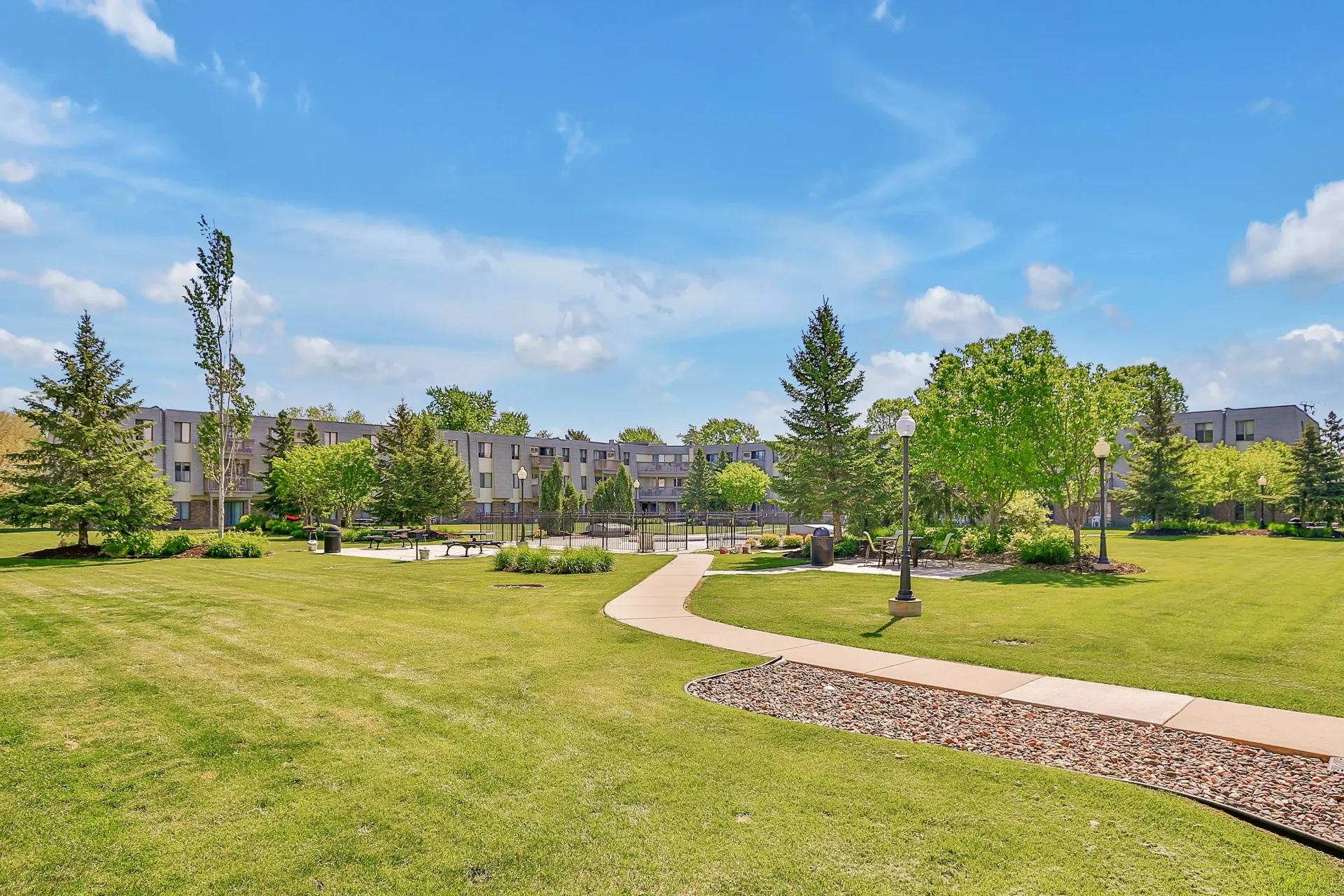 Grassy park with a winding path leading to a building under a blue sky at Eagle Point Apartments in West St. Paul, MN.