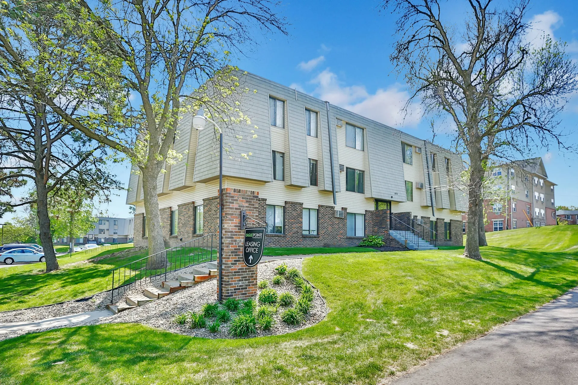 Apartment building exterior with green lawn, trees, and a brick mailbox on a sunny day at Eagle Point Apartments in West St. Paul, MN.