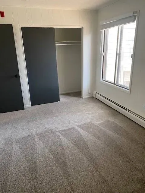 Empty bedroom with gray carpet, closet, two black doors, and a window at Eagle Point Apartments in West St. Paul, MN.