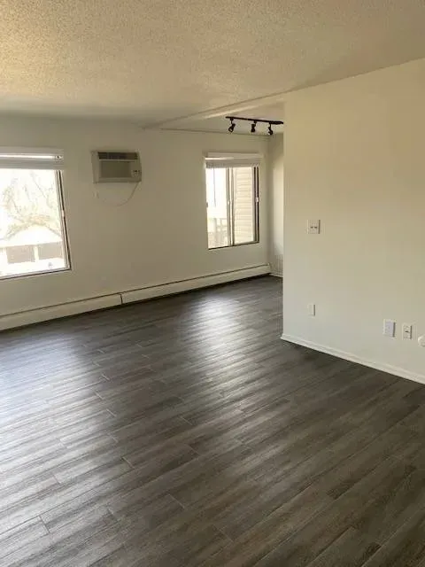 Empty, bright living room with gray flooring, two windows, and an air conditioner at Eagle Point Apartments in West St. Paul, MN.