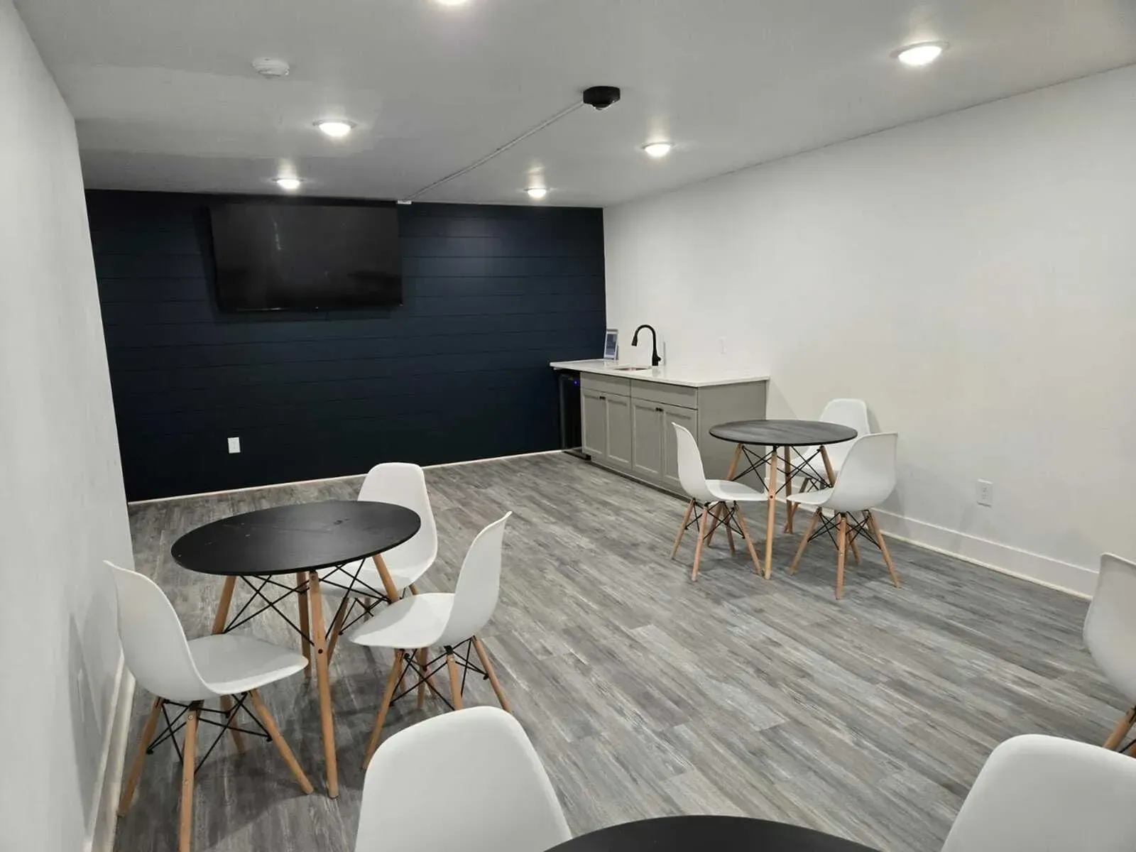 A modern lounge area with white chairs, black tables, gray cabinets, and a dark blue wall with a TV at Eagle Point Apartments in West St. Paul, MN.