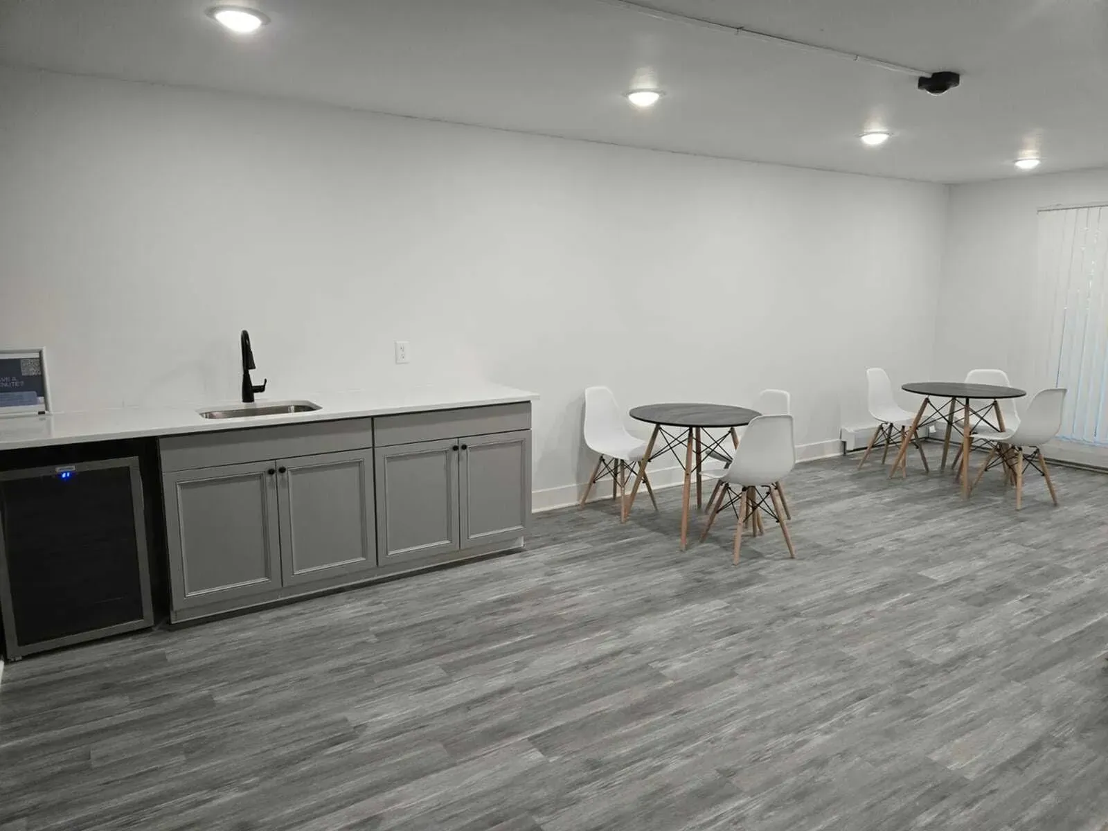 A room with a kitchenette, tables, and chairs. Grey cabinets, white walls, and wooden flooring at Eagle Point Apartments in West St. Paul, MN.