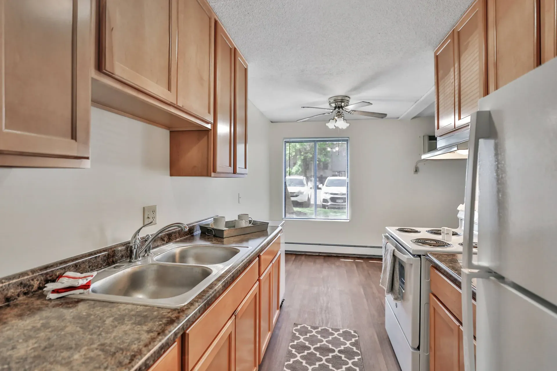 Galley kitchen with a double sink, brown laminate countertops, wooden cabinets, and white refrigerator and stove.