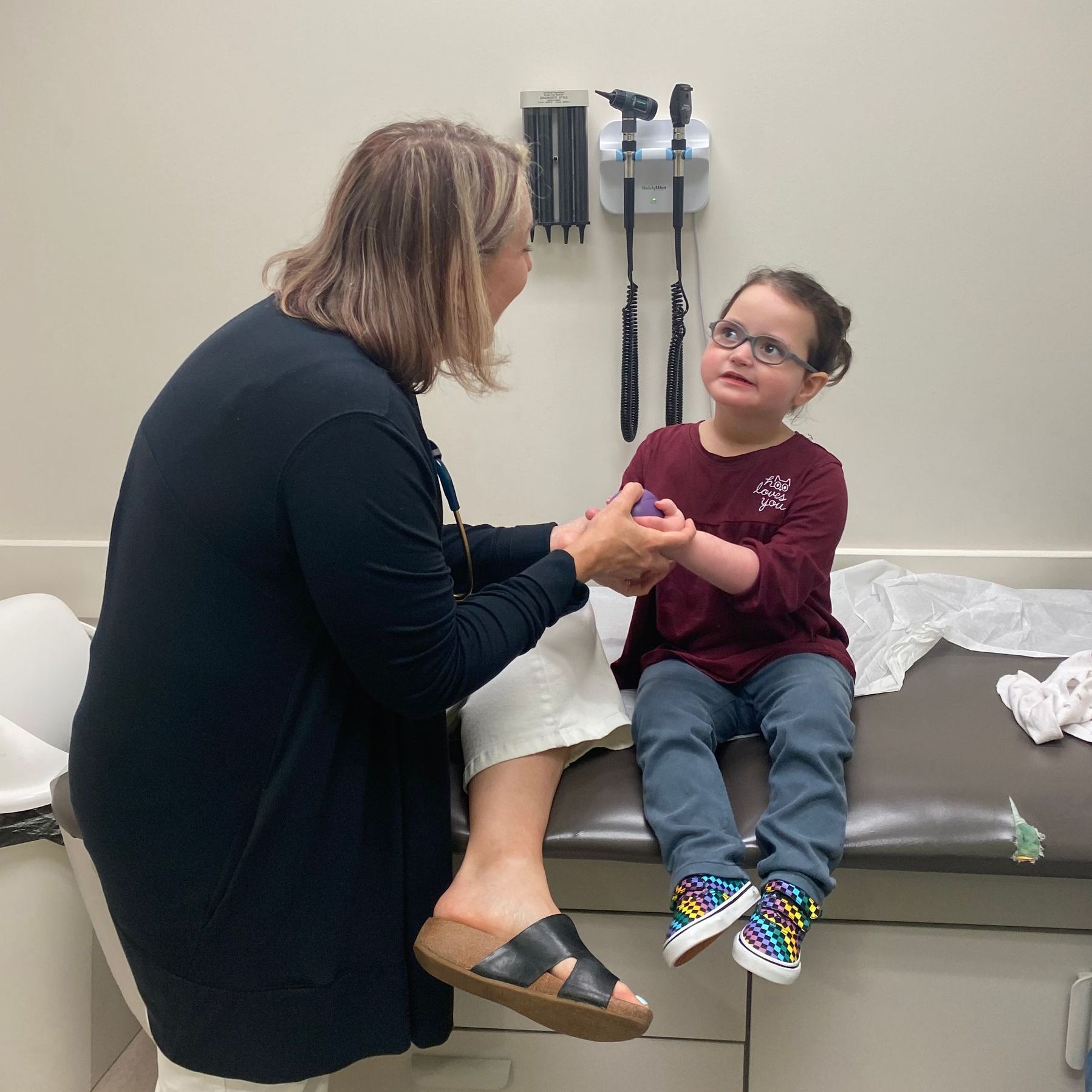A pediatrician is talking to a little girl who is sitting on an exam table