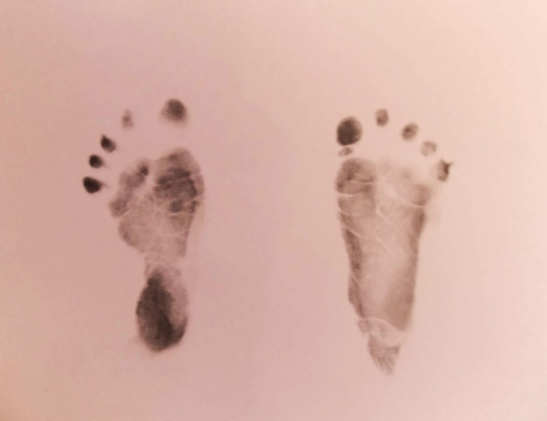 Two footprints of a baby on a pink surface.