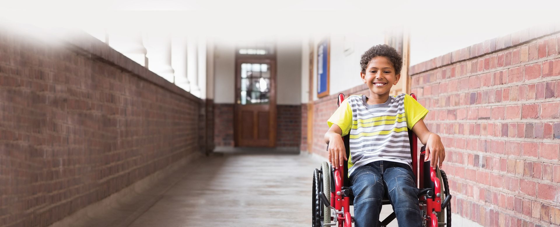 A young boy is sitting in a wheelchair in a hallway.