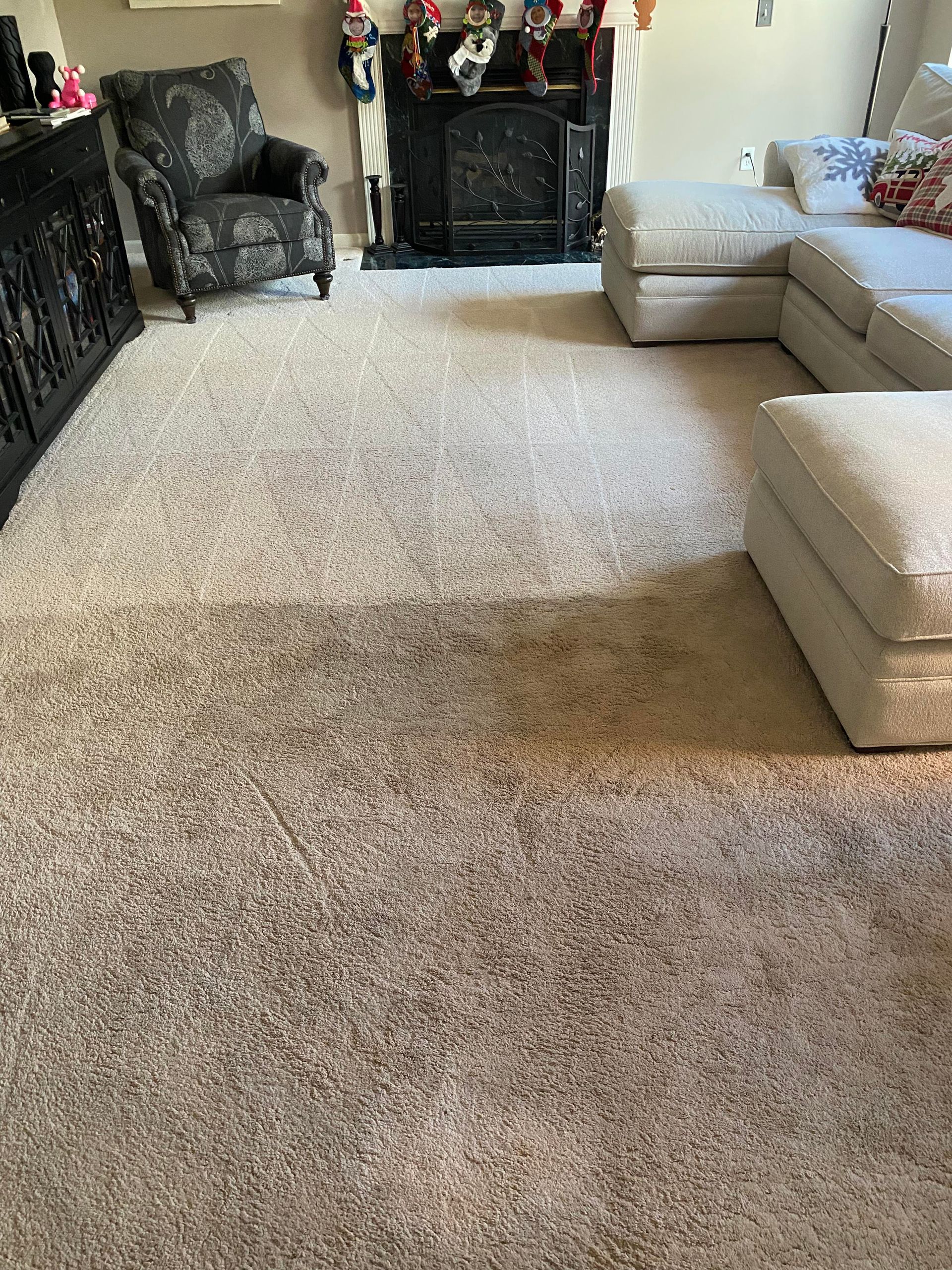 Beige carpet in a living room, with a dark chair, fireplace, and sectional sofa.