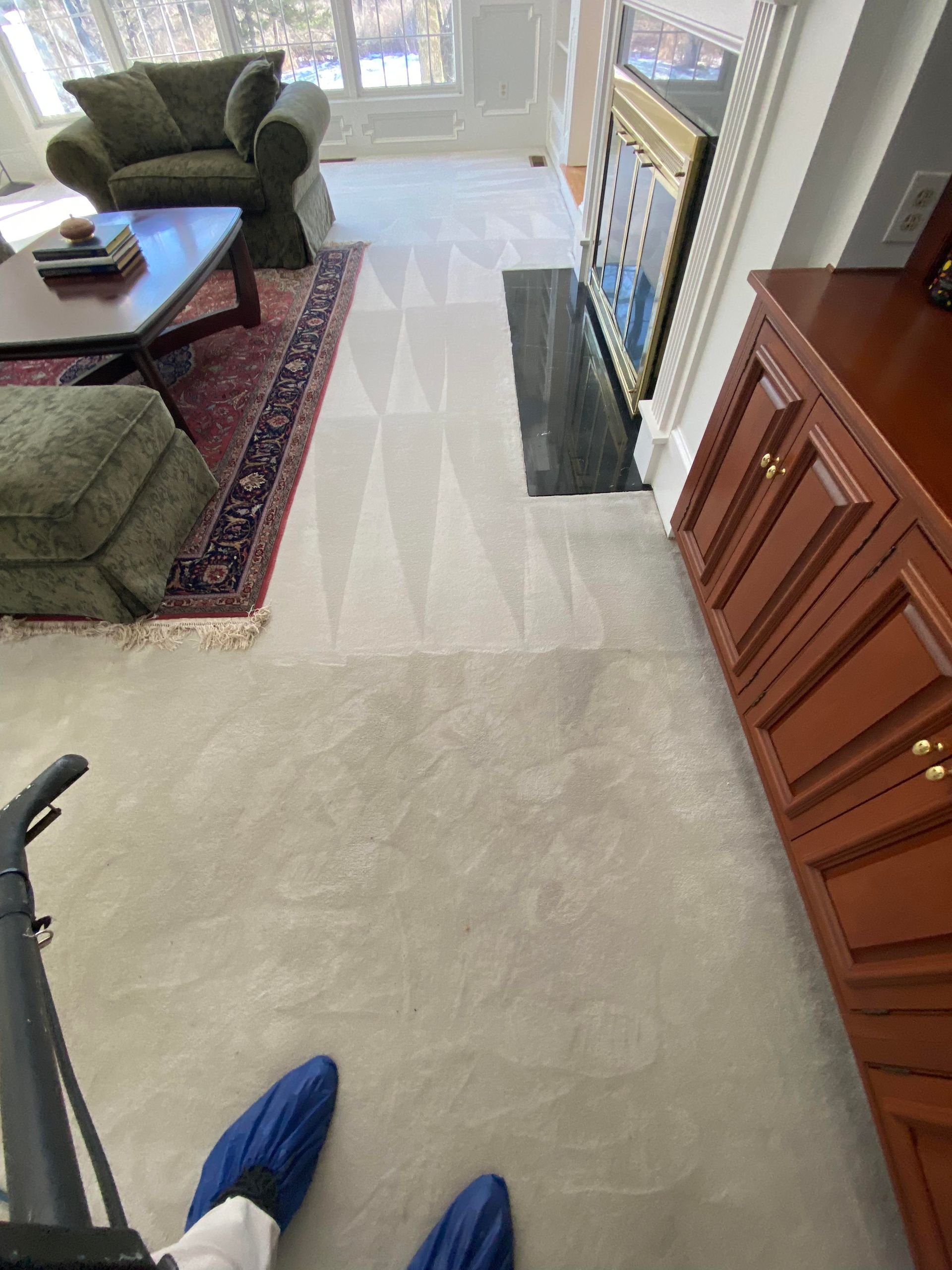 Carpet being cleaned in a living room; a machine and the cleaner's feet are visible.