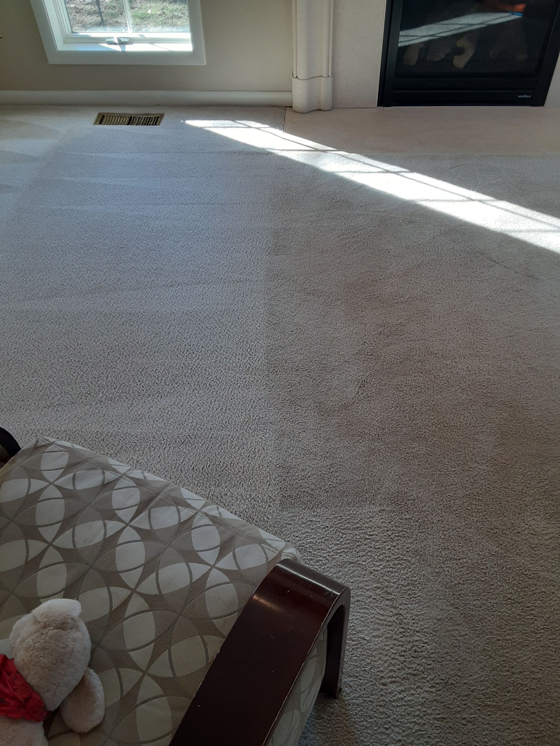 Light-filled room with gray carpet, a patterned chair, fireplace, and window; sunlight streaks across the floor.