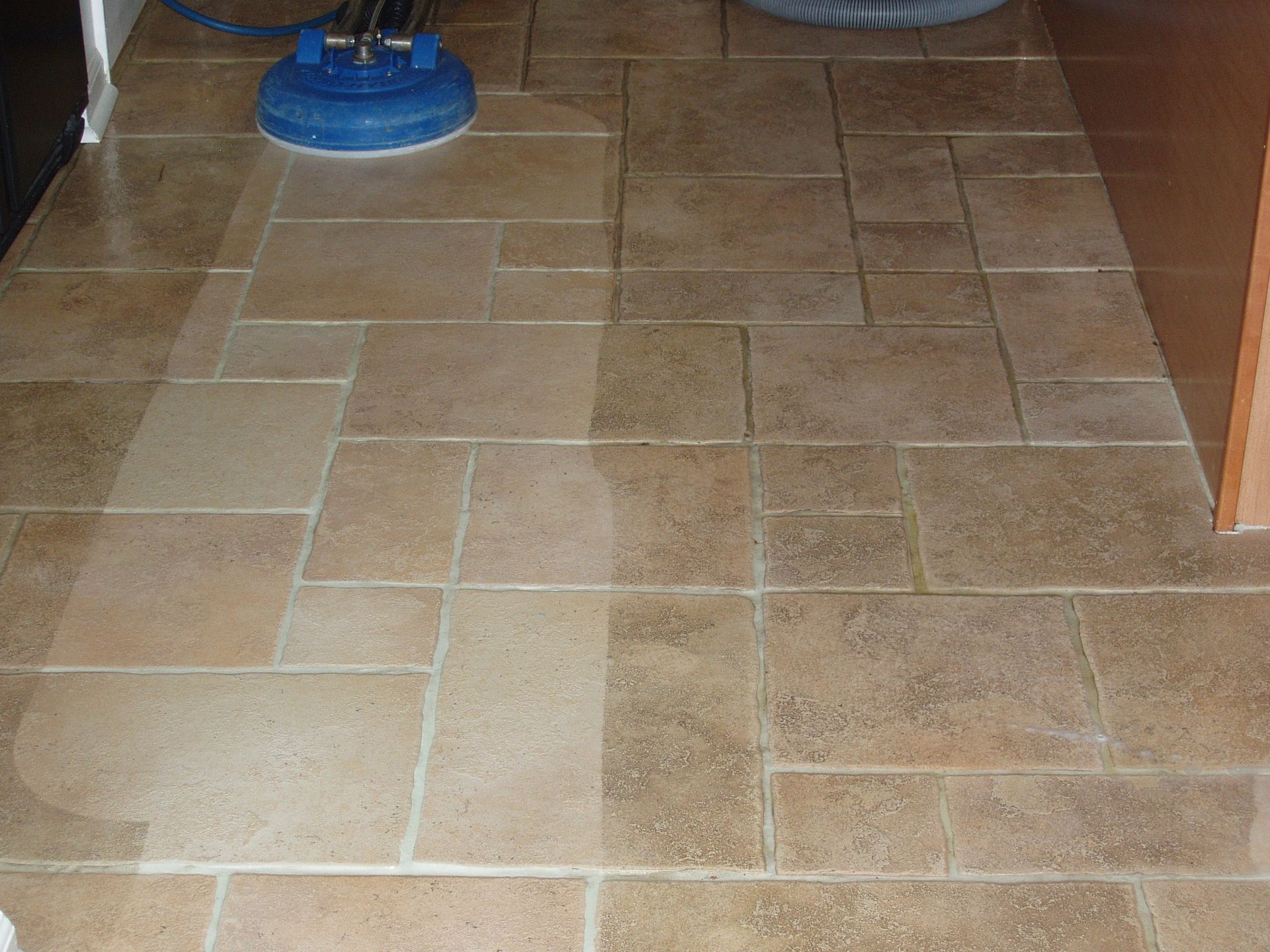 Floor tiles being cleaned with a blue floor buffer; a wet, clean strip is visible.