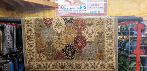 Oriental rug with a beige, red, and blue pattern, hanging in a rug shop.