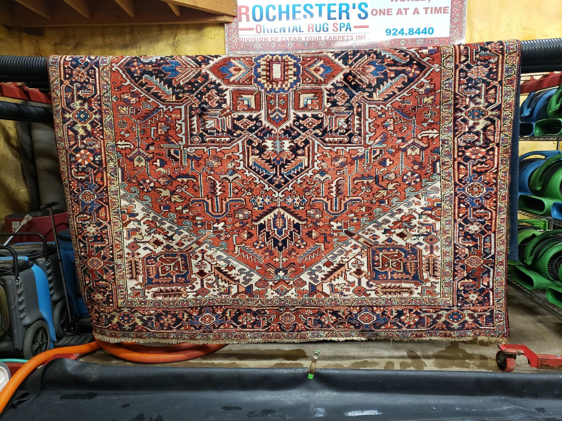 Large, ornate rug with red, blue, and cream patterns hanging in a cleaning facility.