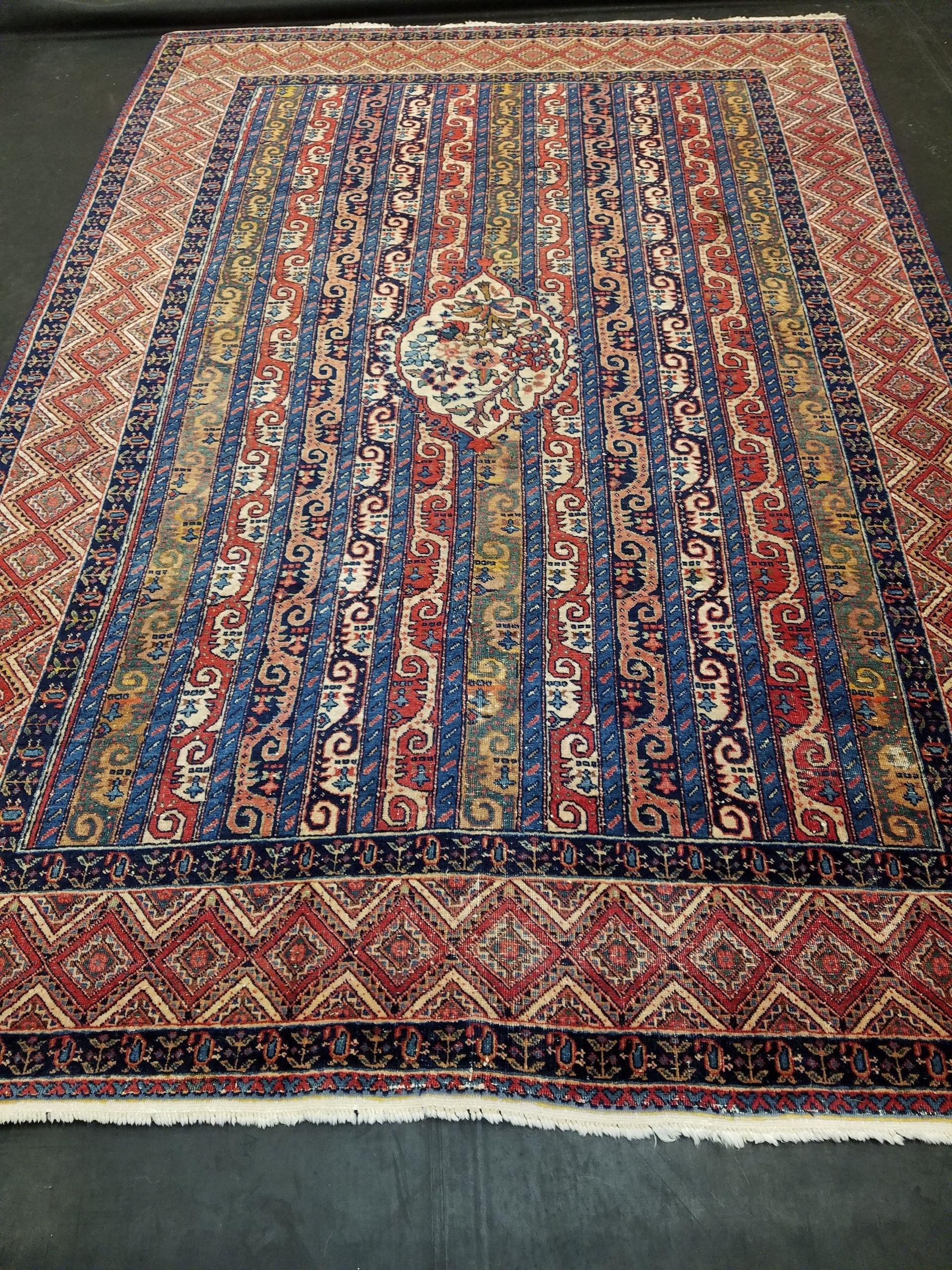 Rectangular Oriental rug with blue, red, and gold vertical stripes, diamond border, and central medallion.