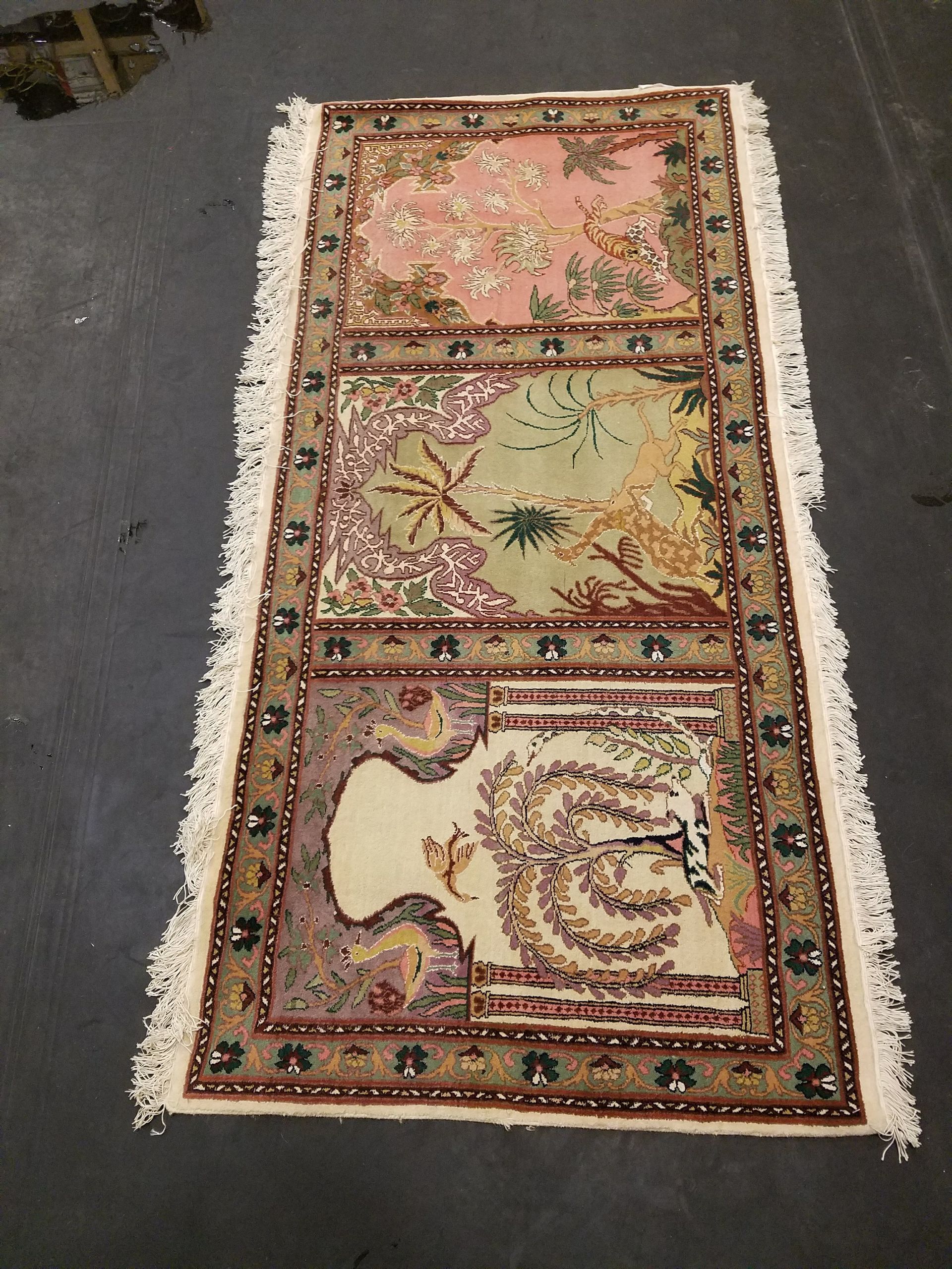 Floral patterned rug with pink, green, and cream panels, framed by a dark border and white fringe.