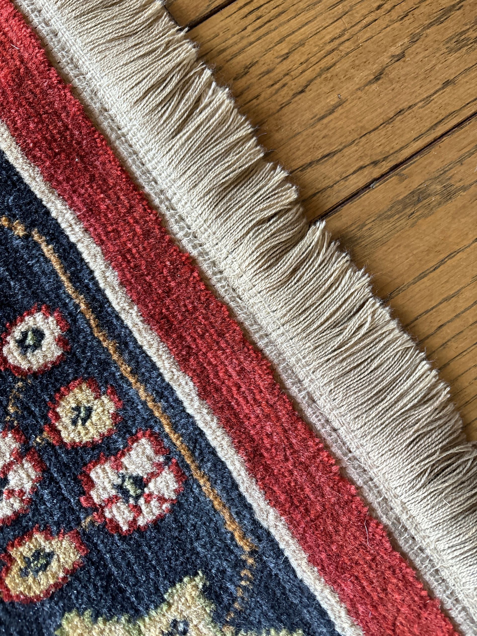 Close-up of a blue and red patterned rug with beige fringe on a wooden floor.