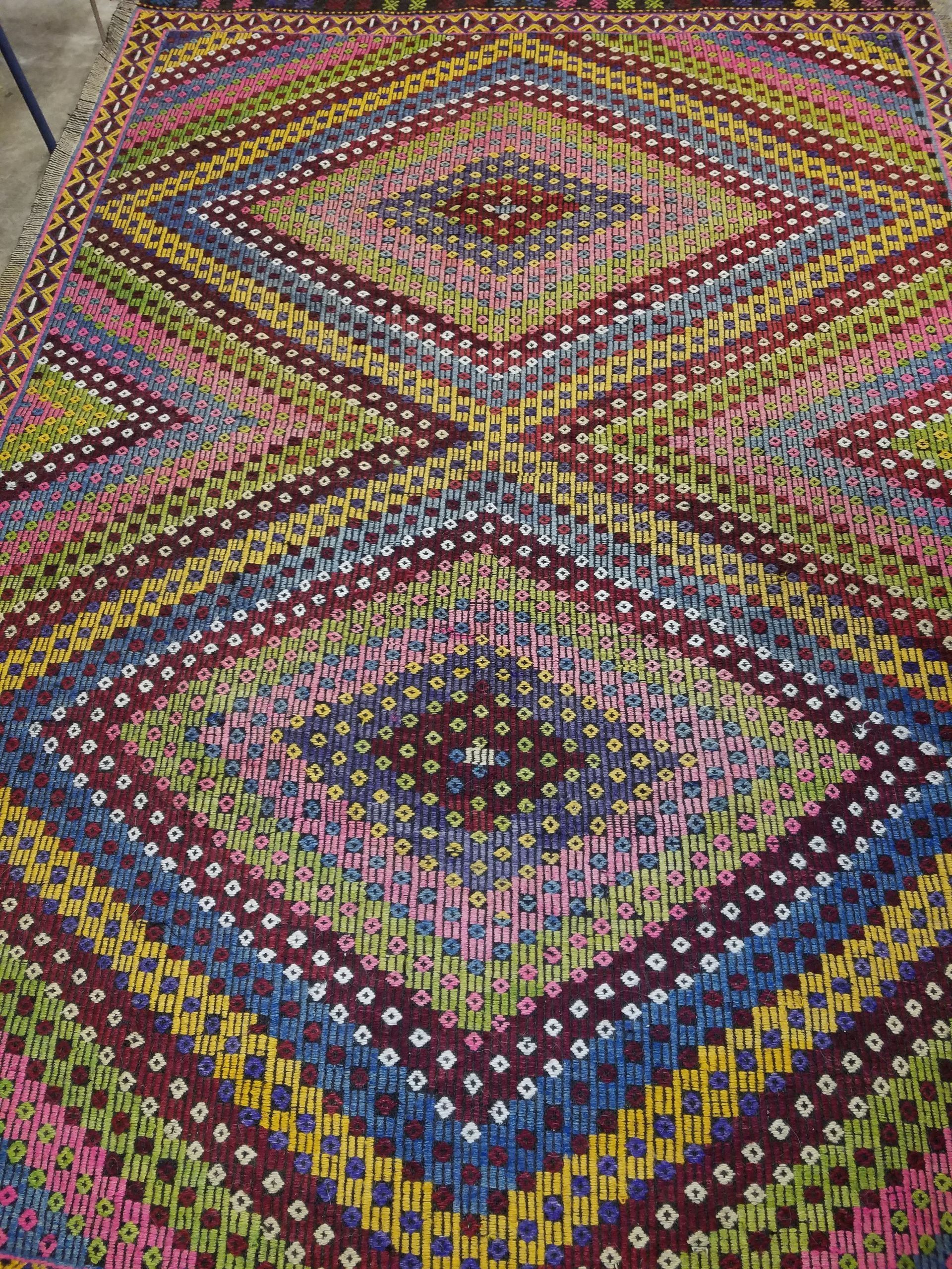 Geometric woven rug with diamond patterns in various colors, including blue, pink, and yellow.